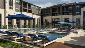 Austin apartment for rent - A pool area with sun loungers and umbrellas in front of a building.